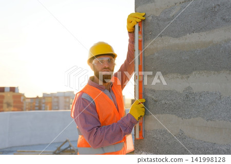 Construction worker using spirit level on building site at sunset Construction worker using spirit level on building site at sunset 141998128