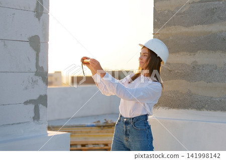 Female engineer measuring wall with tape measure at construction site during sunset Female engineer measuring wall with tape measure at construction site during sunset 141998142