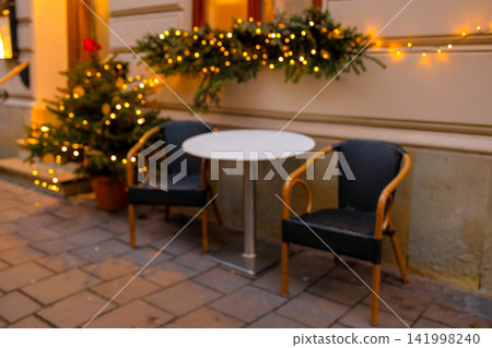 Empty cozy outdoor cafe terrace decorated with Christmas lights at evening Empty cozy outdoor cafe terrace decorated with Christmas lights at evening 141998240