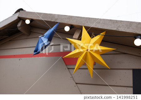 Paper star ornaments hanging on decorated wooden roof at Christmas market Paper star ornaments hanging on decorated wooden roof at Christmas market 141998251