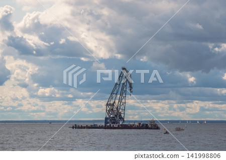 Industrial floating crane barge anchored on the open water under a dramatic cloudy sky. Industrial floating crane barge anchored on the open water under a dramatic cloudy sky. 141998806