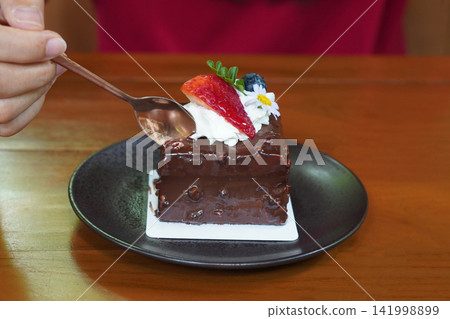 Use a brass spoon to scoop the chocolate cake decorated with a strawberry, a blueberry, and flowers and leaves, brass spoon and fork, placed on a sheet of paper top a black ceramic plate.jpg Use a brass spoon to scoop the chocolate cake decorated with a strawberry, a blueberry, and flowers and leaves, brass spoon and fork, placed on a sheet of paper top a black ceramic plate.jpg 141998899