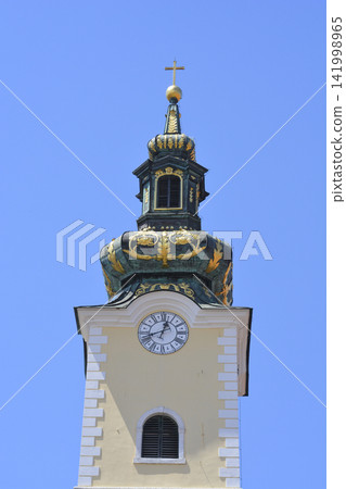 Church tower with a clock and a golden cross against the blue sky Church tower with a clock and a golden cross against the blue sky 141998965