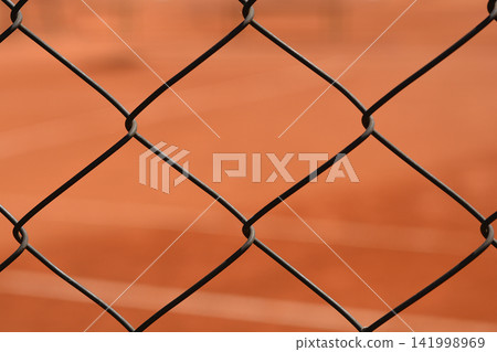 Metal wire mesh fence in front of a red clay tennis court Metal wire mesh fence in front of a red clay tennis court 141998969