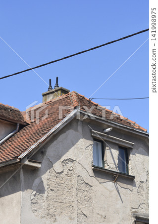 Old house roof with clay tiles and damaged facade Old house roof with clay tiles and damaged facade 141998975