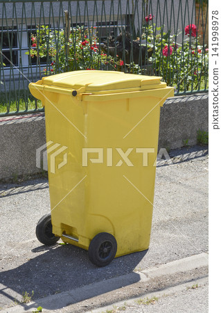 Yellow plastic recycling bin on wheels on a city street Yellow plastic recycling bin on wheels on a city street 141998978
