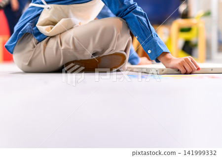 A woman's back as she sits on the floor and arranges a canvas. A woman's back as she sits on the floor and arranges a canvas. 141999332