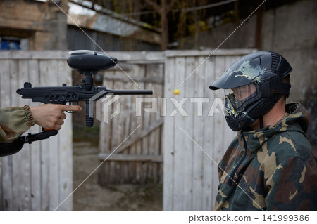 An individual is pointing a military weapon at a soldier wearing a helmet on a field An individual is pointing a military weapon at a soldier wearing a helmet on a field 141999386