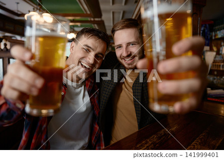 Two white men toasting with beer in closeup selfie in a pub, smiling faces Two white men toasting with beer in closeup selfie in a pub, smiling faces 141999401