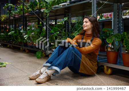 Relaxed female shopper examining foliage display while holding watering can and wearing apron Relaxed female shopper examining foliage display while holding watering can and wearing apron 141999467