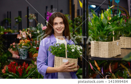 Cheerful caucasian flower seller with basket exhibiting stunning blooms at floral store Cheerful caucasian flower seller with basket exhibiting stunning blooms at floral store 141999484