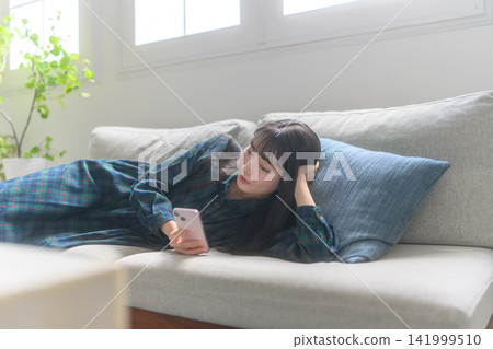 觀看在沙發的婦女一個智能手機 141999510