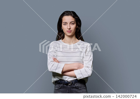 Portrait of a confident 18-year-old young woman with crossed arms on grey background Portrait of a confident 18-year-old young woman with crossed arms on grey background 142000724