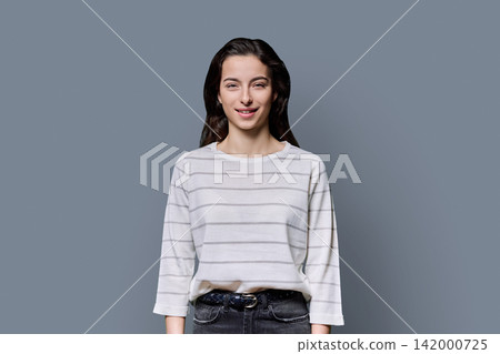 Portrait of a smiling 18-year-old young woman on grey studio background Portrait of a smiling 18-year-old young woman on grey studio background 142000725