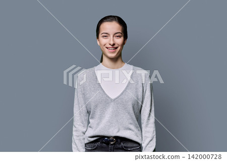 Portrait of a smiling 18-year-old young woman on grey studio background Portrait of a smiling 18-year-old young woman on grey studio background 142000728