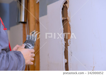 Handyman holds multi tool while cutting through wall in residential area for repair work. 142000852