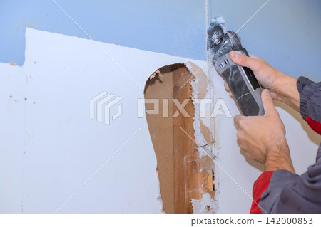 Worker is working on home repair by cutting through wall material with multi tools his takes place indoors in room. 142000853
