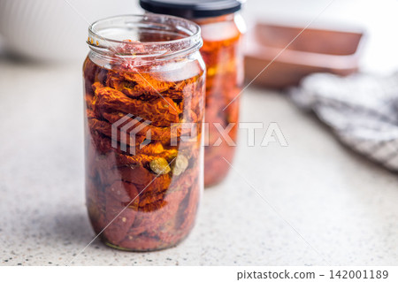 Jar Of Sun-Dried Tomatoes Preserved In Oil On A Kitchen Countertop, Close-Up Jar Of Sun-Dried Tomatoes Preserved In Oil On A Kitchen Countertop, Close-Up 142001189