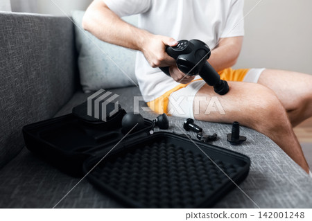 Man uses a massage gun for post-workout recovery and self-massage on his leg. This percussion therapy aids myofascial release, relieves muscle tension, and promotes self-care. Man uses a massage gun for post-workout recovery and self-massage on his leg. This percussion therapy aids myofascial release, relieves muscle tension, and promotes self-care. 142001248