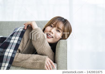 一位年輕女子躺在沙發上,肩上披著圍巾。 一位年輕女子躺在沙發上,肩上披著圍巾。 142001875