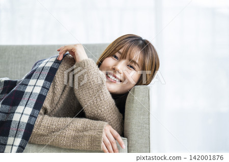 一位年輕女子躺在沙發上,肩上披著圍巾。 一位年輕女子躺在沙發上,肩上披著圍巾。 142001876