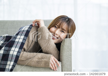 一位年輕女子躺在沙發上,肩上披著圍巾。 一位年輕女子躺在沙發上,肩上披著圍巾。 142001879