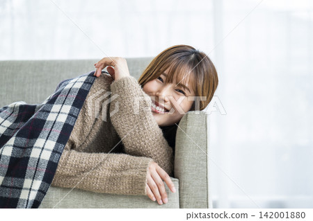 一位年輕女子躺在沙發上,肩上披著圍巾。 一位年輕女子躺在沙發上,肩上披著圍巾。 142001880