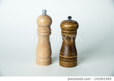 Light wood and dark wood pepper mills, and spice grinders lined up against a white background. Light wood and dark wood pepper mills, and spice grinders lined up against a white background. 142001999