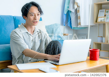 一個男人在客廳裡一邊喝咖啡一邊思考。 一個男人在客廳裡一邊喝咖啡一邊思考。 142002376