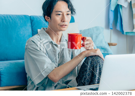 一個男人在客廳裡一邊喝咖啡一邊思考。 一個男人在客廳裡一邊喝咖啡一邊思考。 142002378