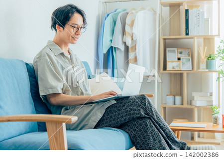 A man working remotely while sitting on a sofa. A man working remotely while sitting on a sofa. 142002386