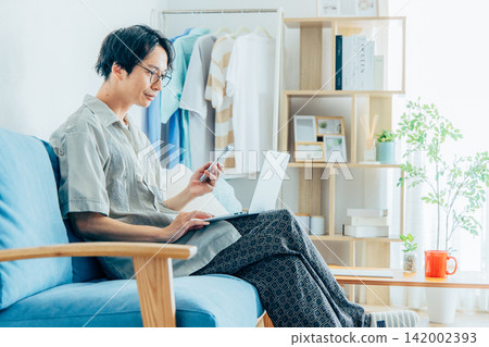 A man working remotely while sitting on a sofa. A man working remotely while sitting on a sofa. 142002393
