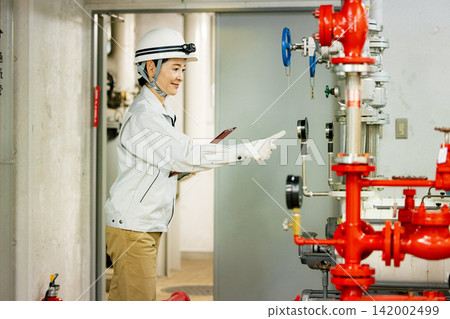 A female worker uses a tablet to inspect equipment in the boiler room. A female worker uses a tablet to inspect equipment in the boiler room. 142002499