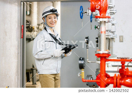 A female worker uses a tablet to inspect equipment in the boiler room. A female worker uses a tablet to inspect equipment in the boiler room. 142002502