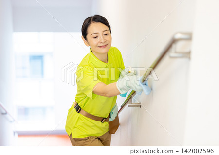 A female staff member in her 50s cleaning the stair railing. A female staff member in her 50s cleaning the stair railing. 142002596