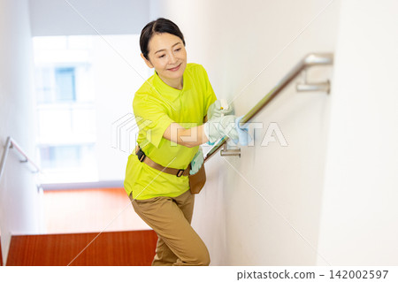 A female staff member in her 50s cleaning the stair railing. A female staff member in her 50s cleaning the stair railing. 142002597