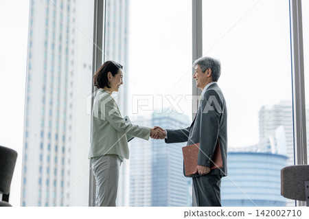 辦公室裡,一對資深生意夥伴(一男一女)握手。 辦公室裡,一對資深生意夥伴(一男一女)握手。 142002710