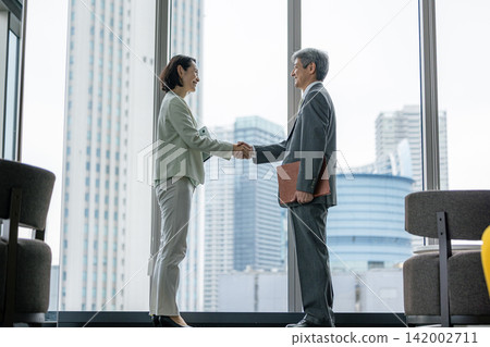 辦公室裡,一對資深生意夥伴(一男一女)握手。 辦公室裡,一對資深生意夥伴(一男一女)握手。 142002711