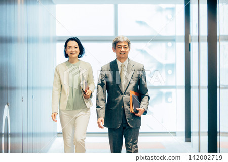 一群上了年紀的男士和女士正在辦公室走廊裡行走,這是一幅商務場景。 一群上了年紀的男士和女士正在辦公室走廊裡行走,這是一幅商務場景。 142002719