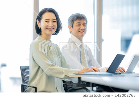 A man and a woman working on laptops in an office. A man and a woman working on laptops in an office. 142002763