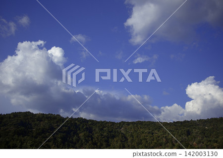 The vast autumn sky stretches above the mountaintop, with lingering summer clouds; the sky's colors are soft. The vast autumn sky stretches above the mountaintop, with lingering summer clouds; the sky's colors are soft. 142003130