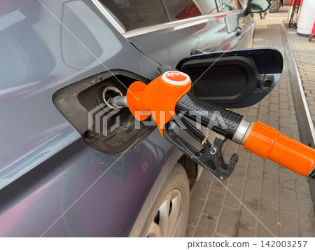 Fuel nozzle is inserted into the gas tank of a car at a service station, with the vehicle body and pavement clearly visible in the background Fuel nozzle is inserted into the gas tank of a car at a service station, with the vehicle body and pavement clearly visible in the background 142003257