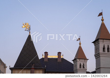 Historic building rooftops display ornate spires and a golden weather vane, set against a clear evening sky with soft lighting Historic building rooftops display ornate spires and a golden weather vane, set against a clear evening sky with soft lighting 142003264