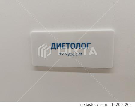 Sign indicating dietitian office with text in Russian and Braille, displayed on a white wall, emphasizing accessibility for all visitors Sign indicating dietitian office with text in Russian and Braille, displayed on a white wall, emphasizing accessibility for all visitors 142003265