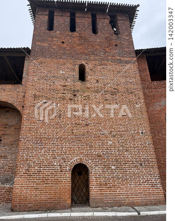 Historic brick tower features an arched doorway and small windows, highlighting weathered brick texture and architectural details under a cloudy sky Historic brick tower features an arched doorway and small windows, highlighting weathered brick texture and architectural details under a cloudy sky 142003347