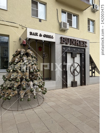 Ryazan, Russia - April 06, 2026: Entrance of a bar and grill featuring a bunker-style door and a tree made of gas masks in an urban environment 142003475