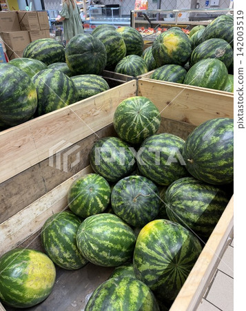 Watermelons are piled in wooden crates at a grocery store, highlighting fresh produce in a colorful market environment Watermelons are piled in wooden crates at a grocery store, highlighting fresh produce in a colorful market environment 142003519