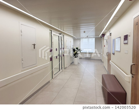 Modern hospital corridor showcases clean design with large windows, potted plant, and patient room doors, featuring a seating area along the walls Modern hospital corridor showcases clean design with large windows, potted plant, and patient room doors, featuring a seating area along the walls 142003520
