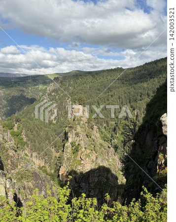 Lush green mountains with rocky cliffs and distant hills are visible under a partly cloudy sky, showcasing a tranquil natural environment Lush green mountains with rocky cliffs and distant hills are visible under a partly cloudy sky, showcasing a tranquil natural environment 142003521
