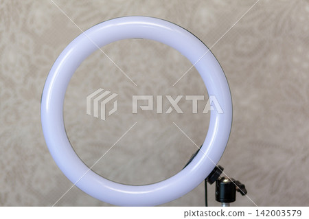 Circular LED ring light mounted on a stand, set against a decorative background, suitable for enhancing photography and video lighting conditions Circular LED ring light mounted on a stand, set against a decorative background, suitable for enhancing photography and video lighting conditions 142003579